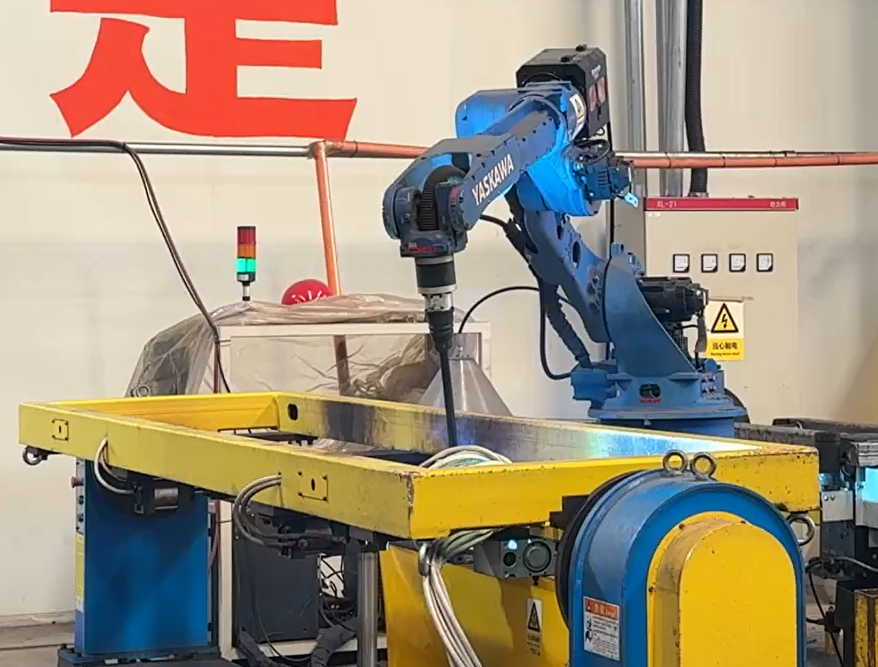 Blue industrial welding robot working over a yellow rotary workpiece fixture